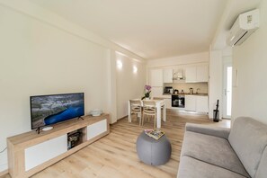 A modern living room with a flat-screen TV, a grey ottoman, and a grey sofa.