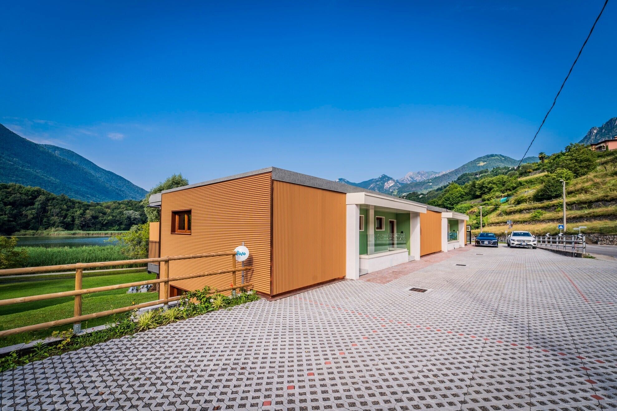 A modern building with a wooden facade, a paved driveway, and a view of mountains.