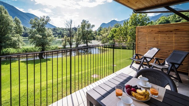 A balcony with a table set for breakfast, overlooking a river and mountains. - Holiday Apartment "3" with Lake View, Shared Pool & Wi-Fi (Carlazzo)
