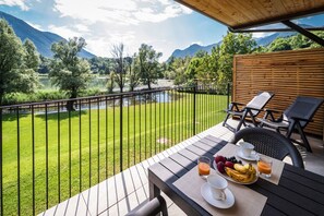 A balcony with a table set for breakfast, overlooking a river and mountains. - Holiday Apartment "3" with Lake View, Shared Pool & Wi-Fi (Carlazzo)