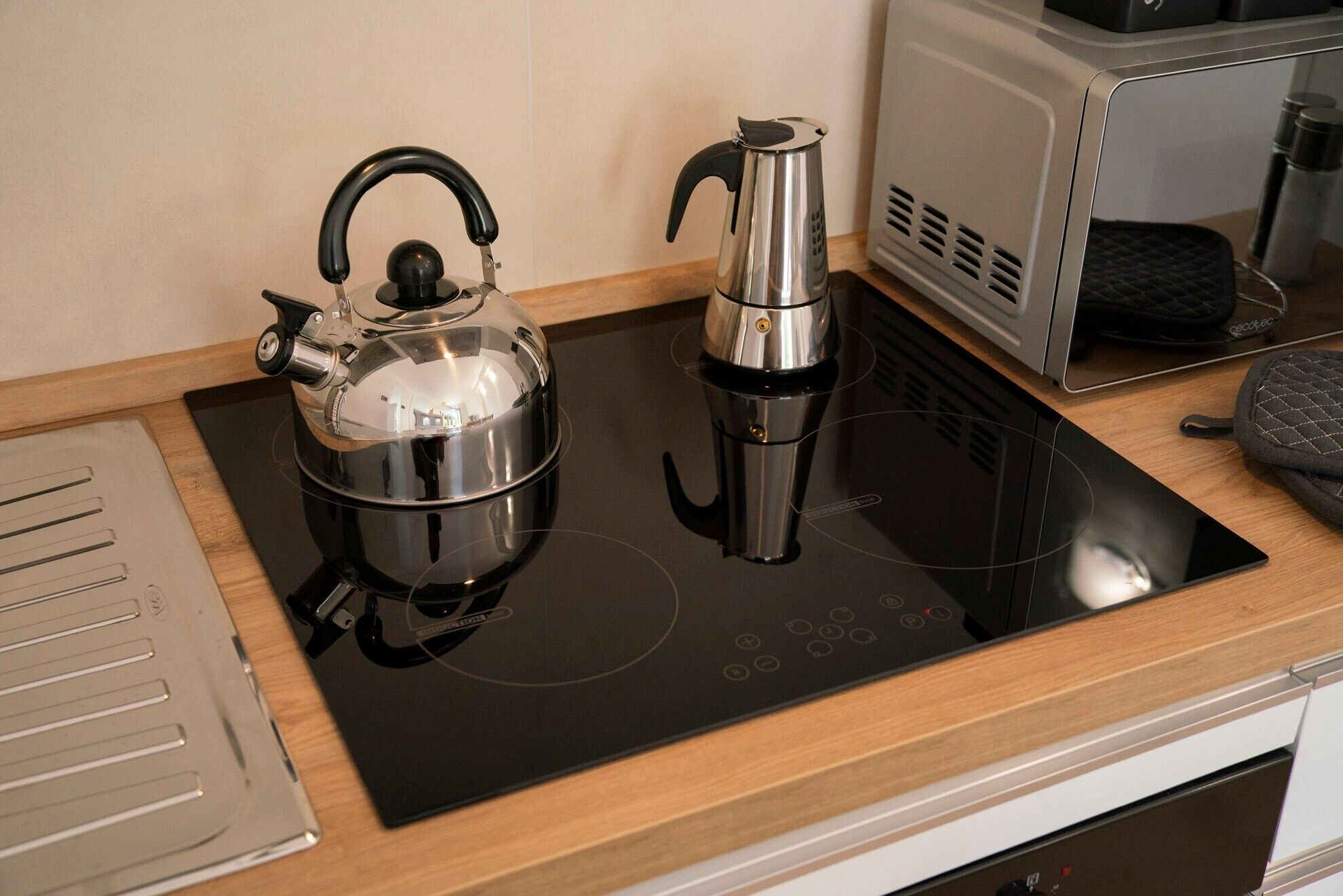 Eine moderne Küche mit einem schwarzen Induktionskochfeld, einem Wasserkocher und einer Kaffeemaschine.