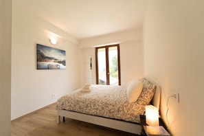 Quarto com cama, abajur, mesa de cabeceira, quadro na parede e janela com vista.