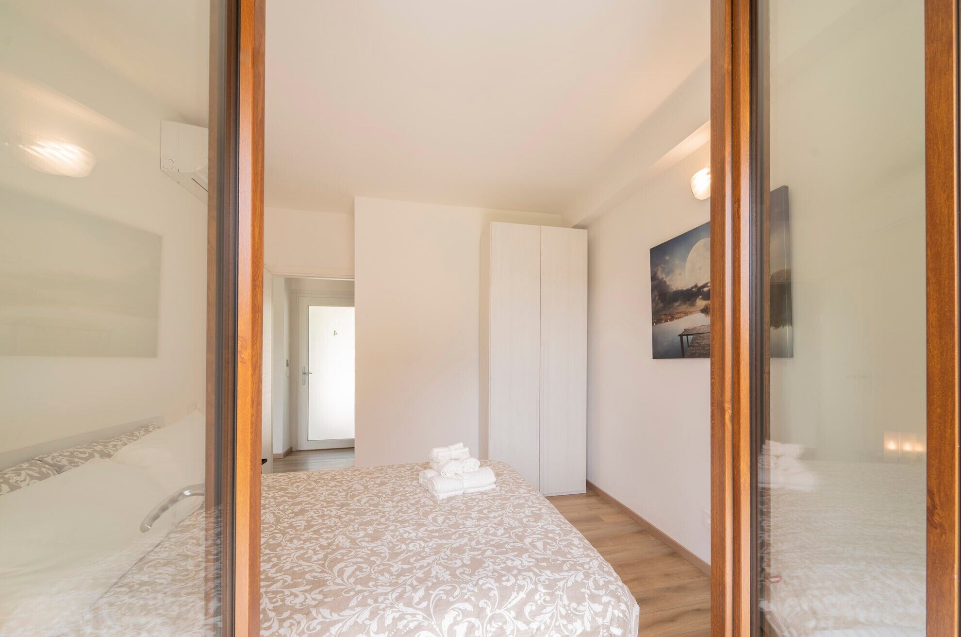 Un dormitorio con cama, armario, un cuadro y una puerta que da a otra habitación.