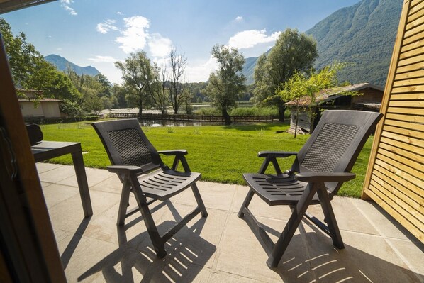 A patio with two chairs and a table, overlooking a grassy area with trees and a mountain in the background.