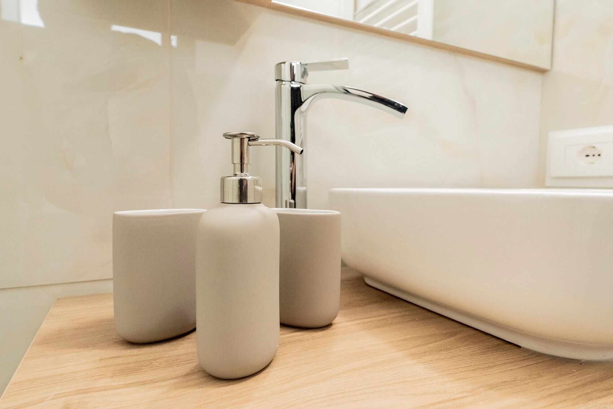 A bathroom with a modern faucet, a bathtub, and two cylindrical containers on a wooden surface.