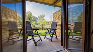 Ein Zimmer mit Glastür, die auf eine Terrasse mit zwei Stühlen und einem Tisch führt, mit Blick auf eine Berglandschaft.
