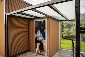 Una entrada de edificio moderna con un muro de listones de madera, una puerta de cristal y vistas a un paisaje verde a través de una ventana.