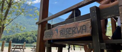 A wooden sign with 'CASA RESERVA' indicating a reserved area, part of a wooden structure with benches, and a view of a lake and mountains in the background.