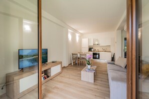 Una sala de estar moderna con televisor, una mesa de centro con revistas, un sofá y una cocina al fondo.