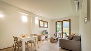 A modern living room with a dining area, a sofa, a TV, and a view of the outdoors. - Holiday Apartment "8" with Lake View, Shared Pool & Wi-Fi (Carlazzo)