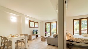 A modern living room with a dining area, a sofa, a TV, and a bed with a view. - Holiday Apartment "8" with Lake View, Shared Pool & Wi-Fi (Carlazzo)