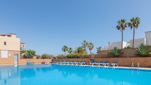 A swimming pool with lounge chairs, palm trees, and a clear sky.