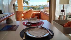 A dining area with a table set for two, a view of the ocean, and a balcony with wicker chairs.