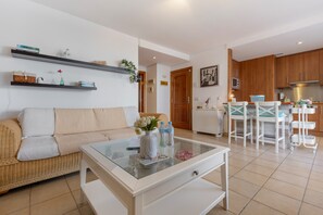 Una sala de estar moderna con una mesa de centro de vidrio, un sofá y una zona de cocina con armarios de madera y un juego de comedor.