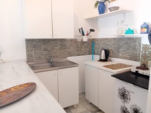Cocina compacta con armarios blancos, un lavamanos de acero inoxidable, un hervidor y una tabla de cortar.