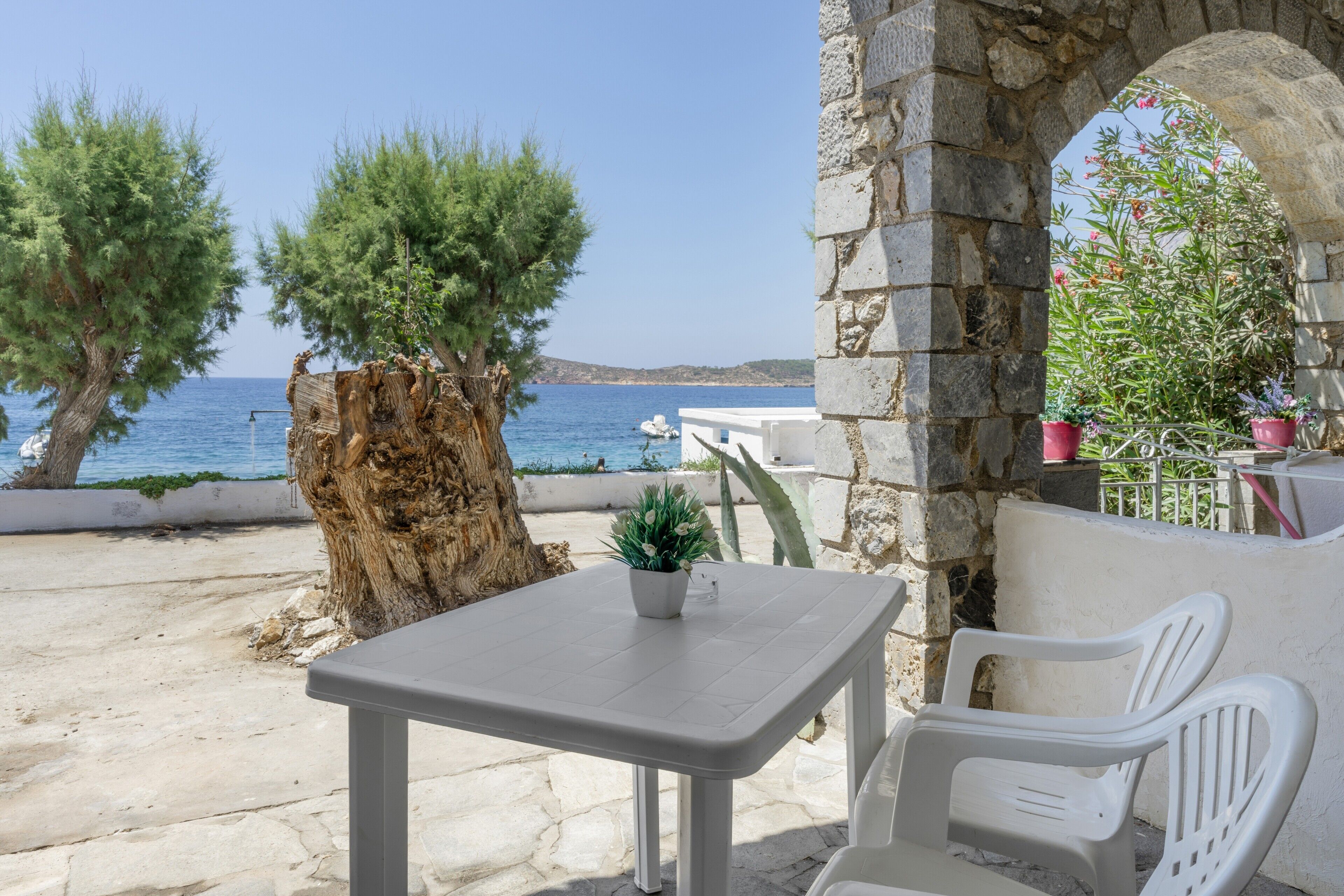 Ein Steintisch mit einem Topfpflanzen, weiße Plastikstühle und Blick aufs Meer.