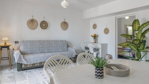 Un salon moderne avec un canapé, des chaises blanches, une table à manger et des éléments décoratifs accrochés au mur.