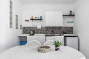 A compact kitchen with white cabinets, a marble backsplash, and a small refrigerator.