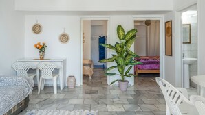 Une chambre comprenant un lit, un bureau avec des chaises, une plante en pot et une salle de bain avec un lavabo et un miroir.