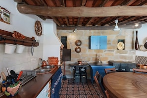 A rustic kitchen with stone walls, wooden beams, a blue table, and a blue cabinet.