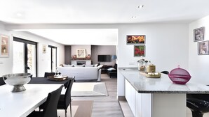 A modern hotel room with a large bed, a dining area, a kitchen, and a living area.
