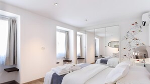 A modern hotel room with a large bed, a mirror, a bedside table, and a view of the outdoors.