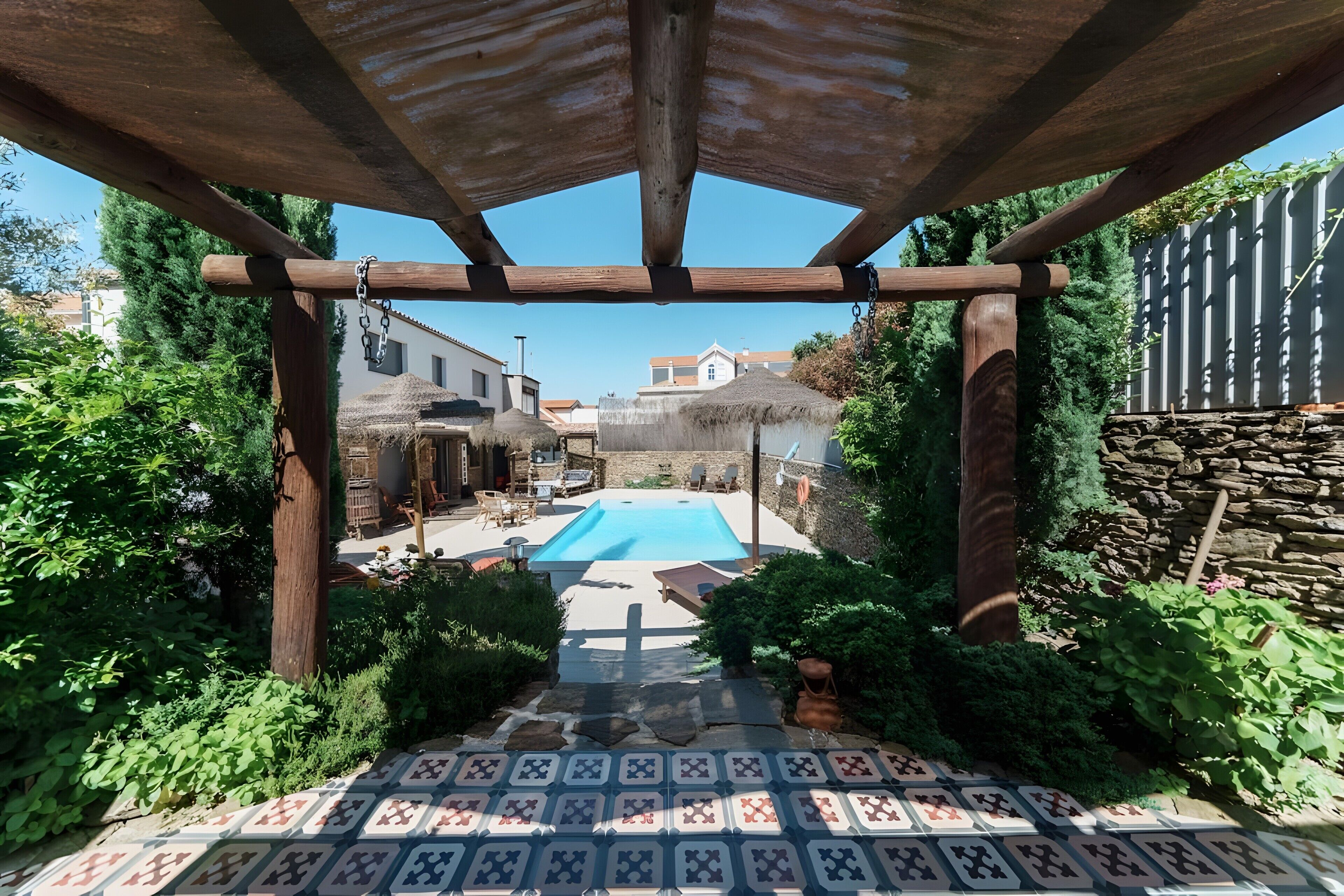 Un espace piscine agrémenté d’une pergola, d’un mur en pierre et d’un toit de chaume.