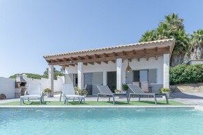 Un área junto a la piscina con sillones de descanso y una pérgola.