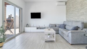A modern living room with a grey sofa, a white coffee table, and a flat-screen TV mounted on the wall. - Villa 'El Olivar 2' with Mountain Views, Wi-Fi and Air Conditioning (Barbate)
