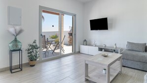 A modern living room with a sofa, coffee table, TV, and a sliding glass door leading to an outdoor area. - Villa 'El Olivar 2' with Mountain Views, Wi-Fi and Air Conditioning (Barbate)