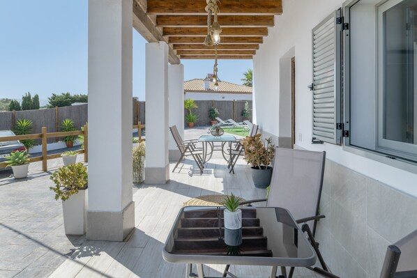 A covered patio area with a wooden ceiling, a table with chairs, and potted plants.