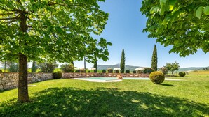 A well-maintained lawn with a swimming pool, stone walls, and trees.