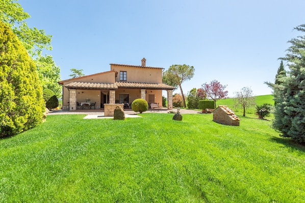 Une maison à deux étages dotée d’un patio, entourée d’une pelouse bien entretenue et de divers arbres.
