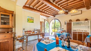 A spacious dining area with wooden furniture, a blue tablecloth, and a view through large windows.
