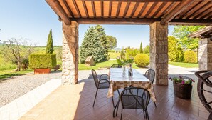 An outdoor patio with a table and chairs, stone pillars, and a view of a landscaped garden.