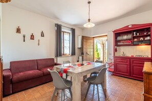 Zona de menjador amb taula, cadires, un sofà vermell i cuina amb armaris vermells.