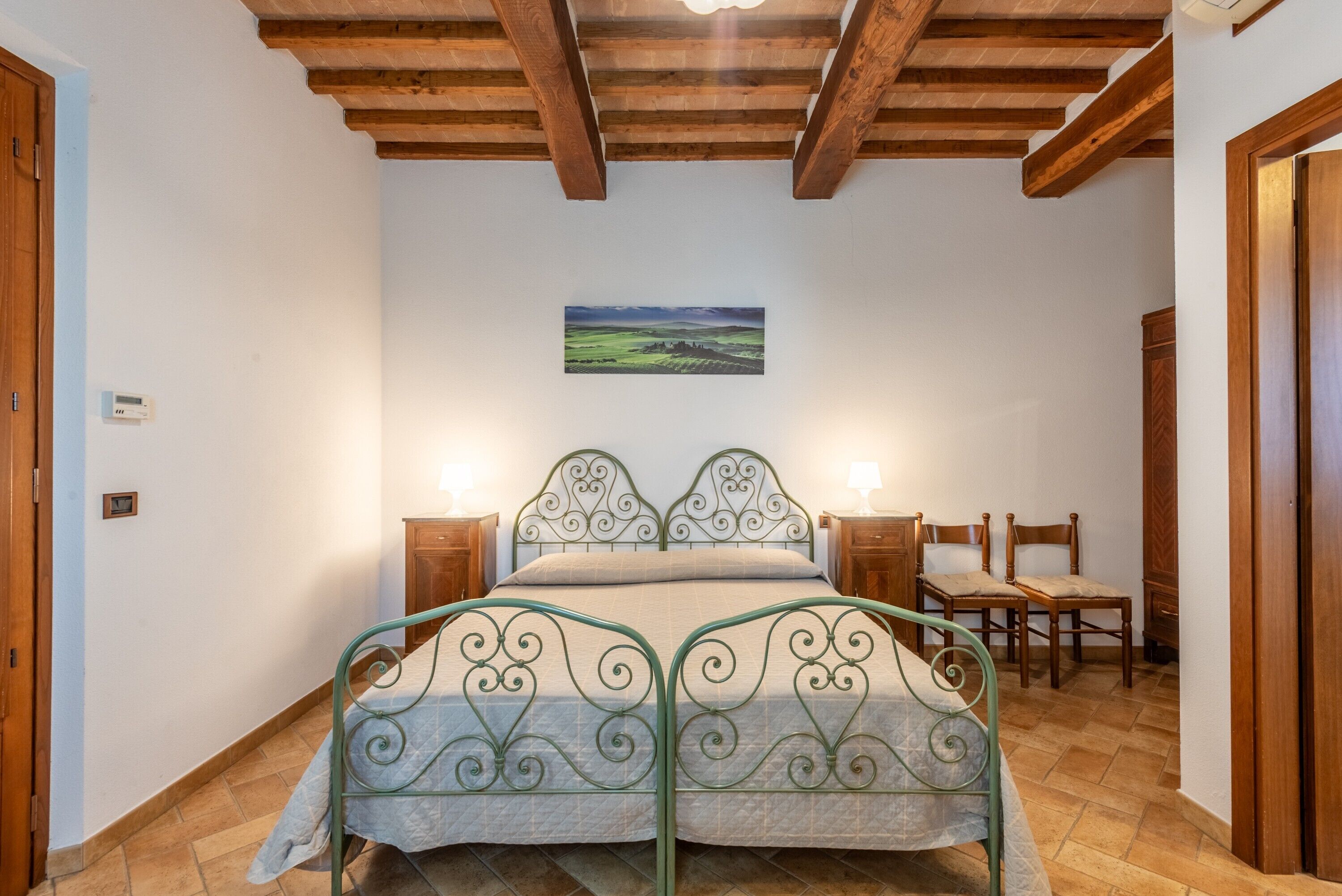 Une chambre à coucher avec un lit en métal, des poutres apparentes en bois au plafond, une table de chevet avec une lampe et une chaise.