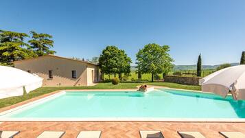 Una piscina con lettini e ombrelloni, circondata da un edificio e alberi.