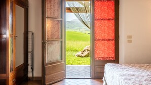 A room with a bed, a wooden wardrobe, a radiator, and a door leading to a green landscape. - Apartment 'La Casina' with Shared Pool, Wi-Fi and Air Conditioning (Castiglione d'Orcia)