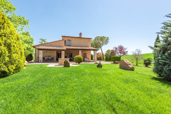 Une maison à deux étages dotée d’un patio, entourée d’une pelouse bien entretenue et de divers arbres.