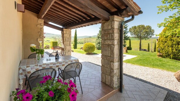 An outdoor patio with a table and chairs, stone pillars, and a view of the countryside.