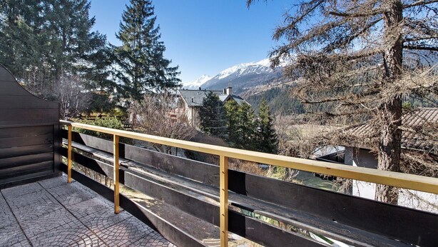 En balkon med trægelænder der vender ud mod et bjergrigt landskab.