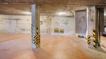 An underground parking area with concrete pillars, a tiled floor, and a wall with graffiti.