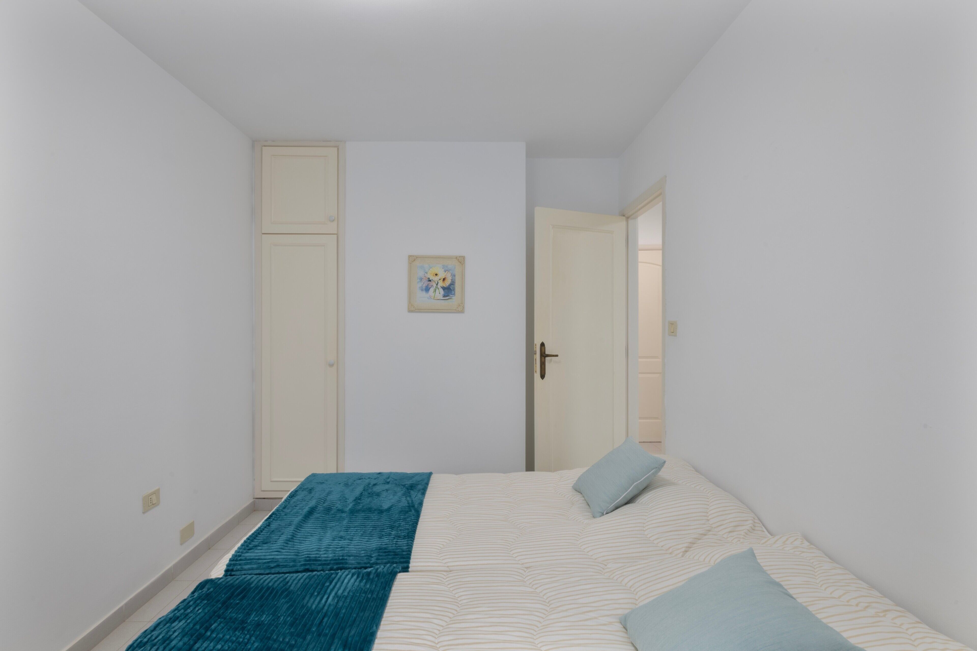 A bedroom with two beds, a door, and a small painting on the wall.