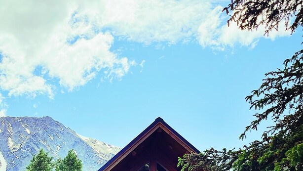 A log cabin with a balcony, large windows, and a mountain backdrop.