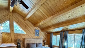 A cozy attic bedroom with a wooden ceiling, a bed, a desk, and a chair.