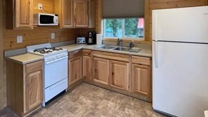 Une cuisine compacte dotée de meubles en bois, d’une cuisinière, d’un four à micro-ondes, d’un réfrigérateur et d’une fenêtre donnant sur un espace verdoyant.