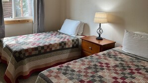 Une chambre avec deux lits, chacun recouvert d’une courtepointe, une table de chevet avec une lampe et une fenêtre avec des rideaux.