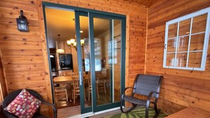 A wooden cabin interior with a dining area, a television, and a sliding glass door leading to a kitchen. - Lakefront Home on the Whitefish Chain - Outdoor Pool, Pickleball Courts and More (Pequot Lakes)