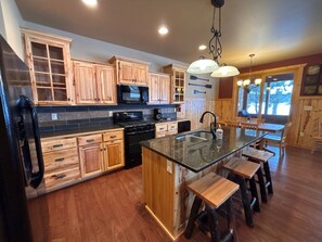 A kitchen with wooden cabinets, a black stove, a sink, and a bar area with stools. - Lakefront Home on the Whitefish Chain - Outdoor Pool, Pickleball Courts and More (Pequot Lakes)